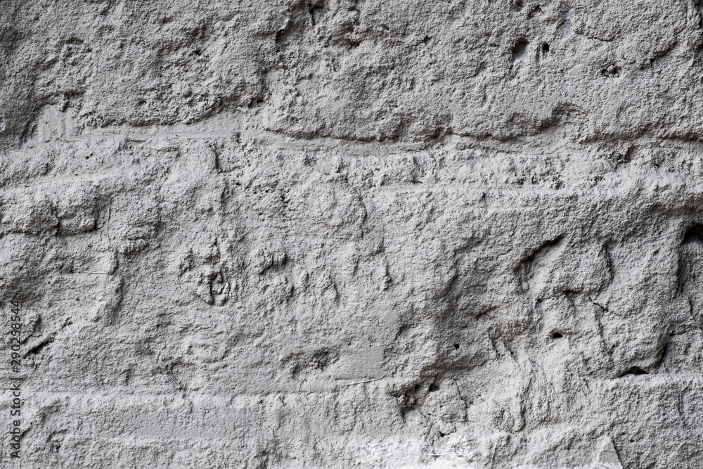 Gray uneven stone wall with broken plaster. Grunge background.