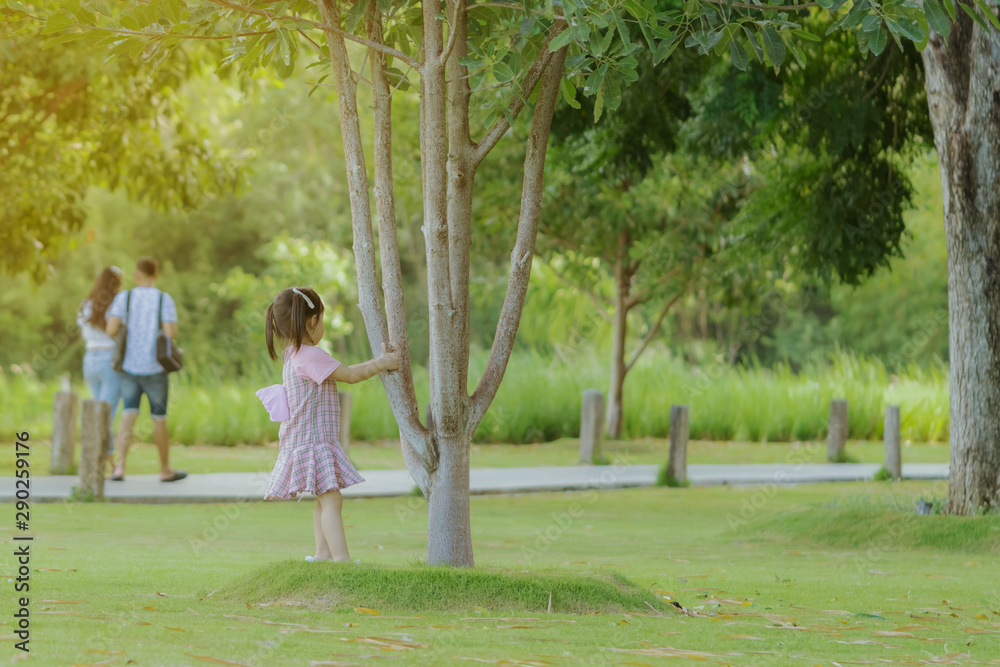 Fototapeta premium A little girl in a pink skirt enjoys a relaxing time playing on the green lawn at the public park in the evening.