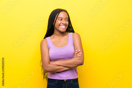 African American teenager girl with long braided hair over isolated yellow wall happy and smiling