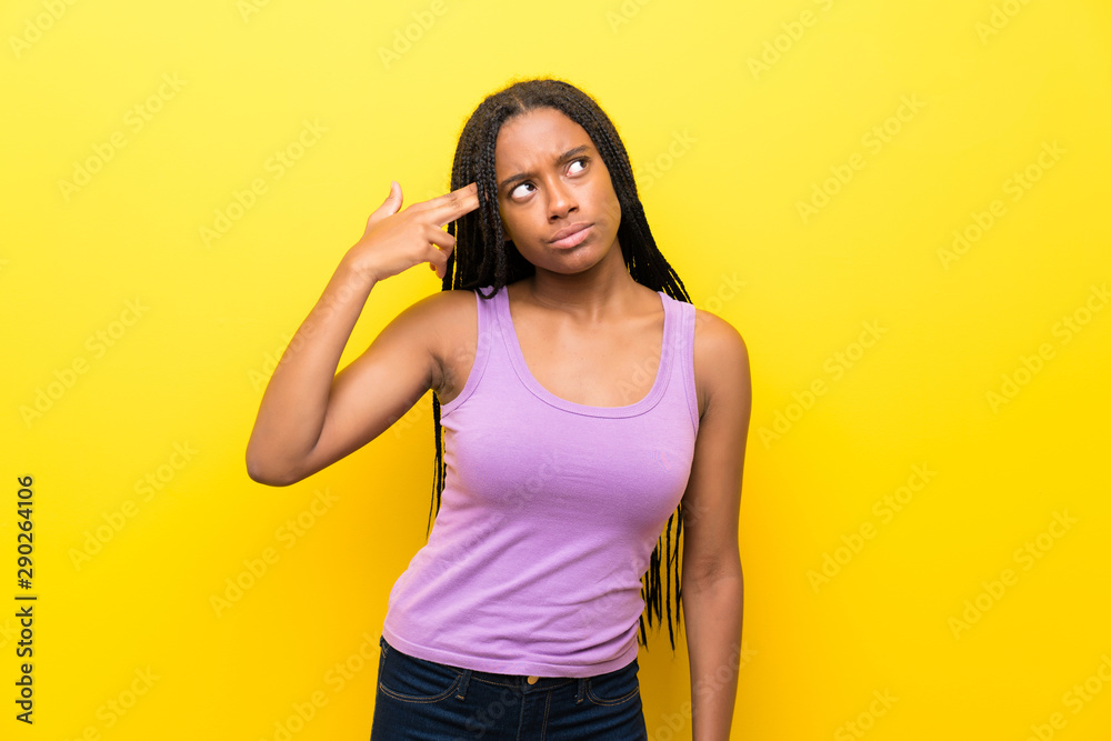 African American teenager girl with long braided hair over isolated yellow wall with problems making suicide gesture African American teenager girl with long braided hair over isolated yellow wall with problems making suicide gesture
