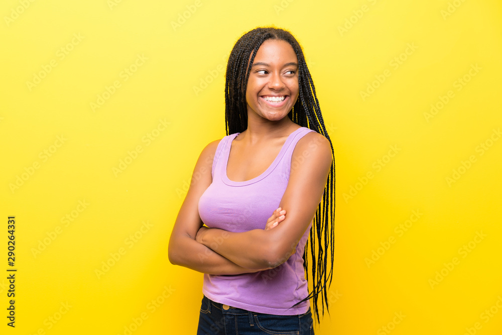 Obraz premium African American teenager girl with long braided hair over isolated yellow wall with arms crossed and happy