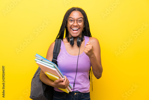 African American teenager student girl with long braided hair over isolated yellow wall celebrating a victory