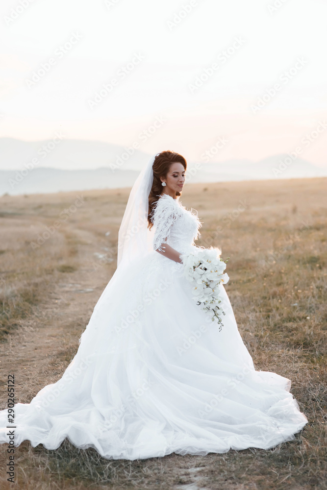 Beautiful young bride is holding a wonderful bouquet of orchid. She is wearing a white wedding dress, girl turned back. Very beautifu with lush white lace dress on your wedding day. Beautiful woman.