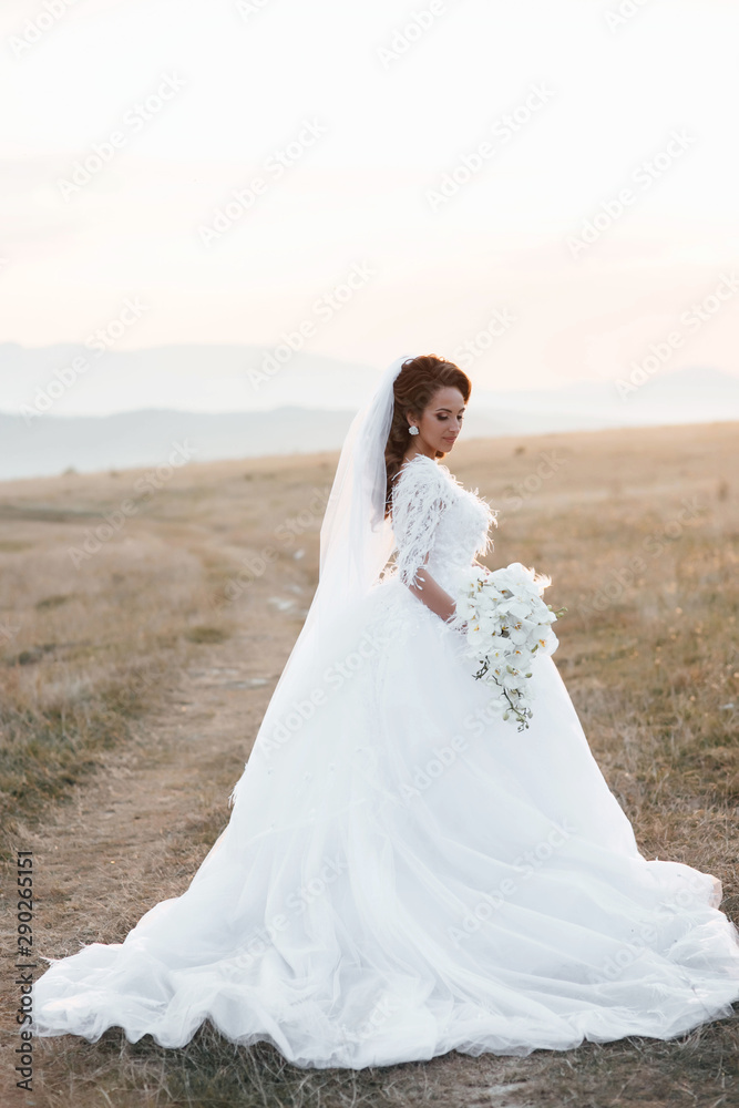 Beautiful young bride is holding a wonderful bouquet of orchid. She is wearing a white wedding dress, girl turned back. Very beautifu with lush white lace dress on your wedding day. Beautiful woman.