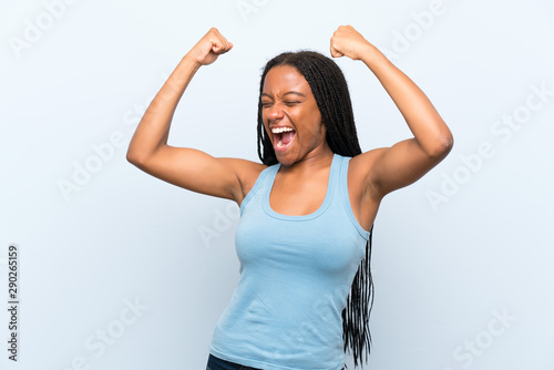 African American teenager girl with long braided hair over isolated blue background celebrating a victory