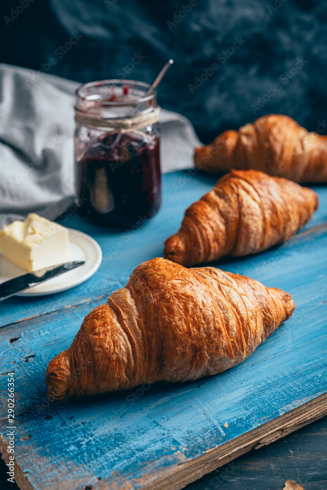 tasty croissants, butter and plum jam on blue wooden table