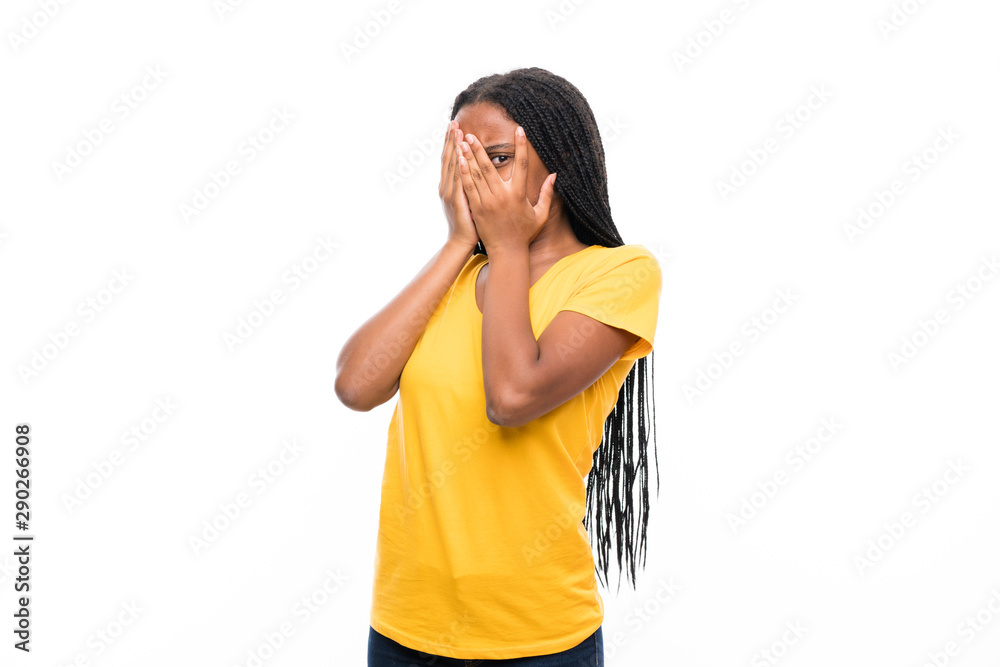 African American teenager girl with long braided hair over isolated white background covering eyes and looking through fingers