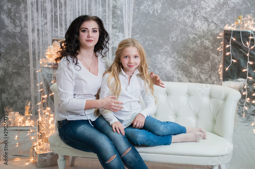 Two very pretty girls, sisters celebrates Christmas, new year. Girls in the New Year's interior of the room are sitting on a white sofa against the background of garlands