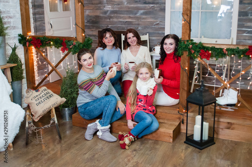 Several very pretty women and a teenager girl celebrate Christmas, the new year. Girls in the New Year's interior with cups in their hands are sitting on the steps © queen1987