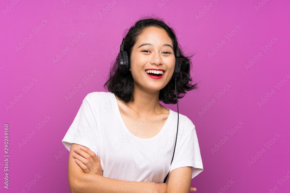 Fototapeta premium Asian young girl listening music with a mobile and singing over isolated purple wall