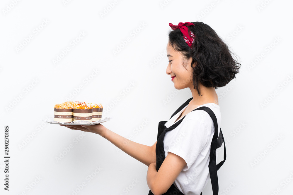 Young asian girl holding lots of muffin cake over isolated white background with happy expression Young asian girl holding lots of muffin cake over isolated white background with happy expression