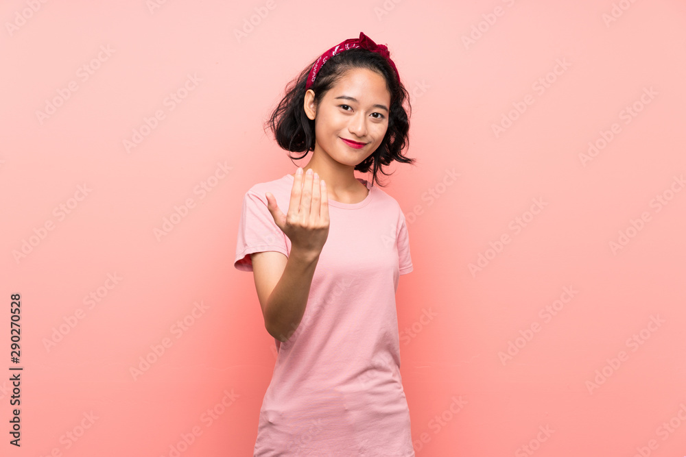 Asian young woman over isolated pink background inviting to come with hand. Happy that you came Asian young woman over isolated pink background inviting to come with hand. Happy that you came