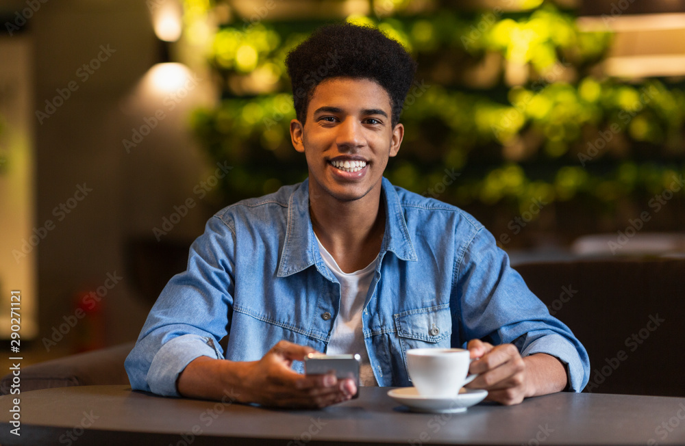Cheerful black teen guy drinking coffee at cafeteria