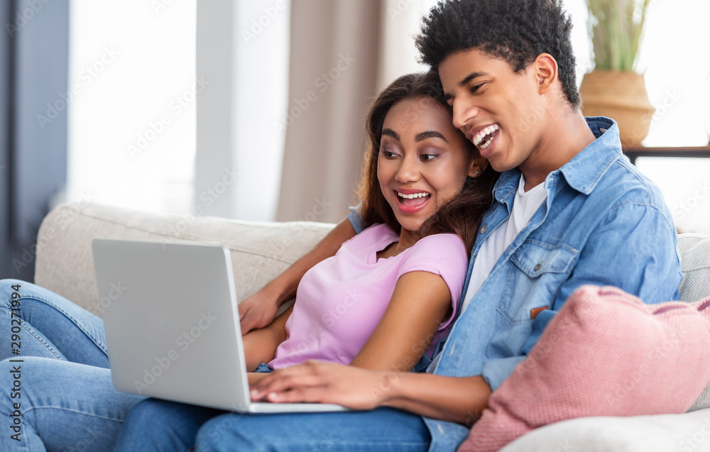 Smiling millennial couple watching funny video on laptop at home
