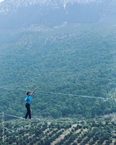 A man is walking along a stretched sling. Highline in the mountains. Man catches balance. Performance of a tightrope walker in nature. Highliner on the background of the mountains.