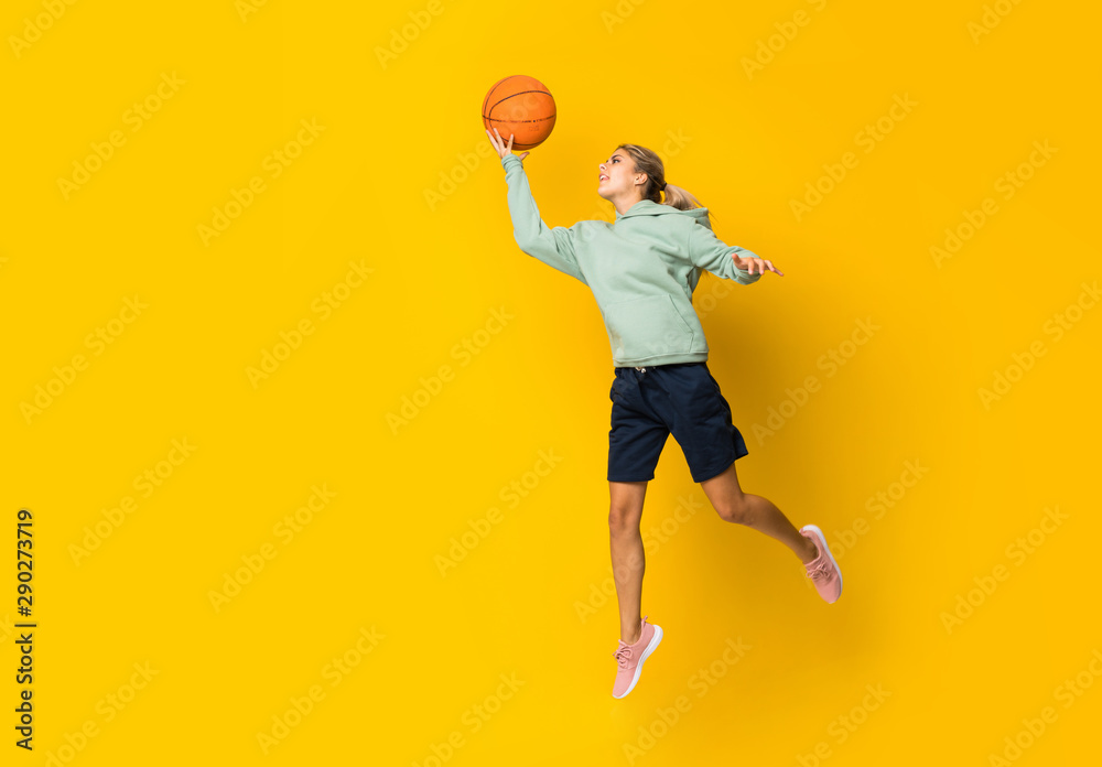 Teenager girl basketball ball jumping over isolated yellow background. - obrazy, fototapety, plakaty 