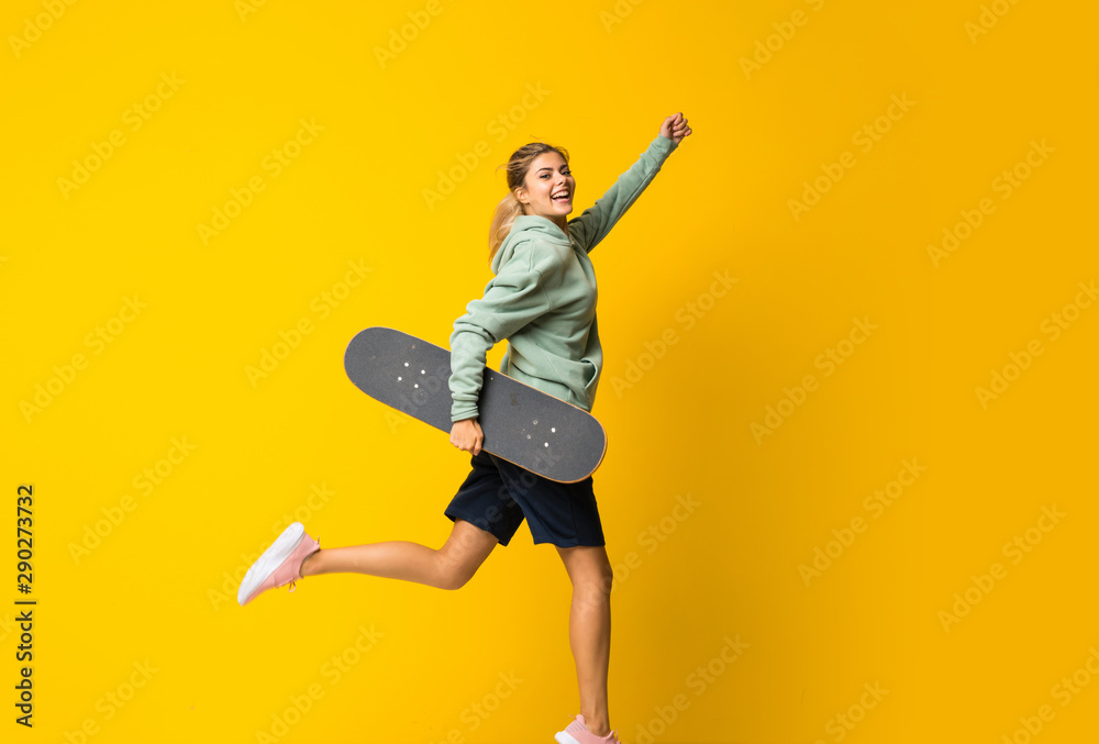 Obraz premium Blonde teenager skater girl jumping over isolated yellow background