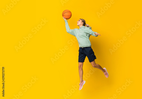 Teenager girl basketball ball jumping over isolated yellow background.