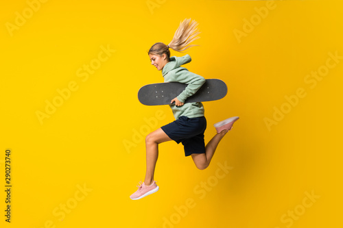 Blonde teenager skater girl jumping over isolated yellow background photo