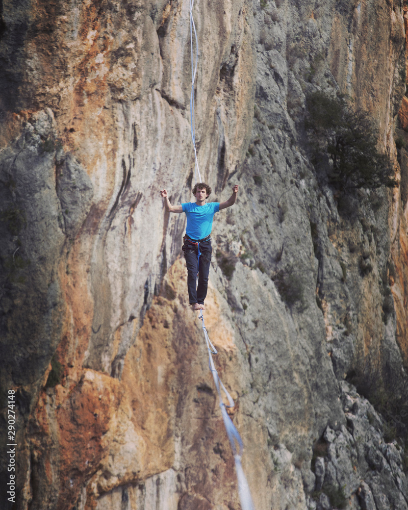 A man is walking along a stretched sling. Highline in the mountains. Man catches balance. Performance of a tightrope walker in nature. Highliner on the background of the mountains.