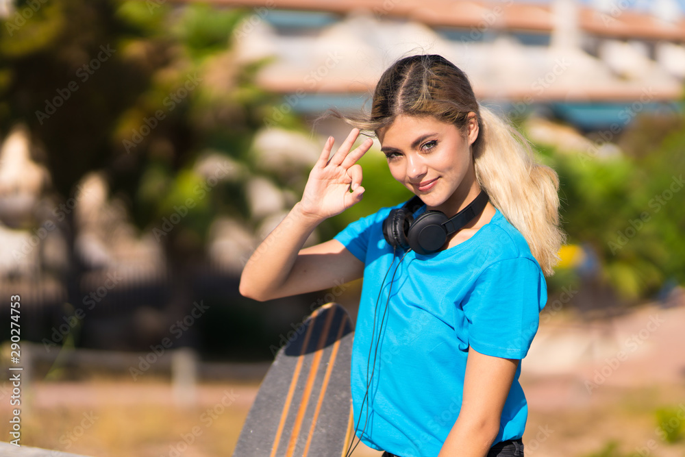 Teenager girl with skate at outdoors showing ok sign with fingers Teenager girl with skate at outdoors showing ok sign with fingers