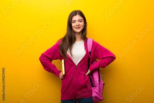 Teenager student girl on vibrant yellow background posing with arms at hip