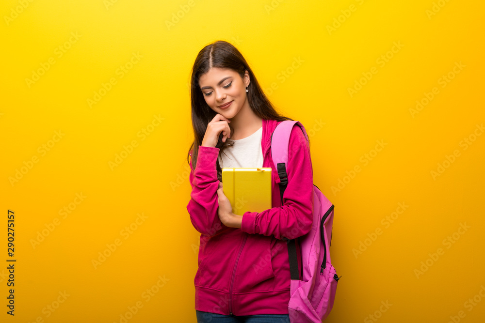 Teenager student girl on vibrant yellow background standing and looking down Teenager student girl on vibrant yellow background standing and looking down