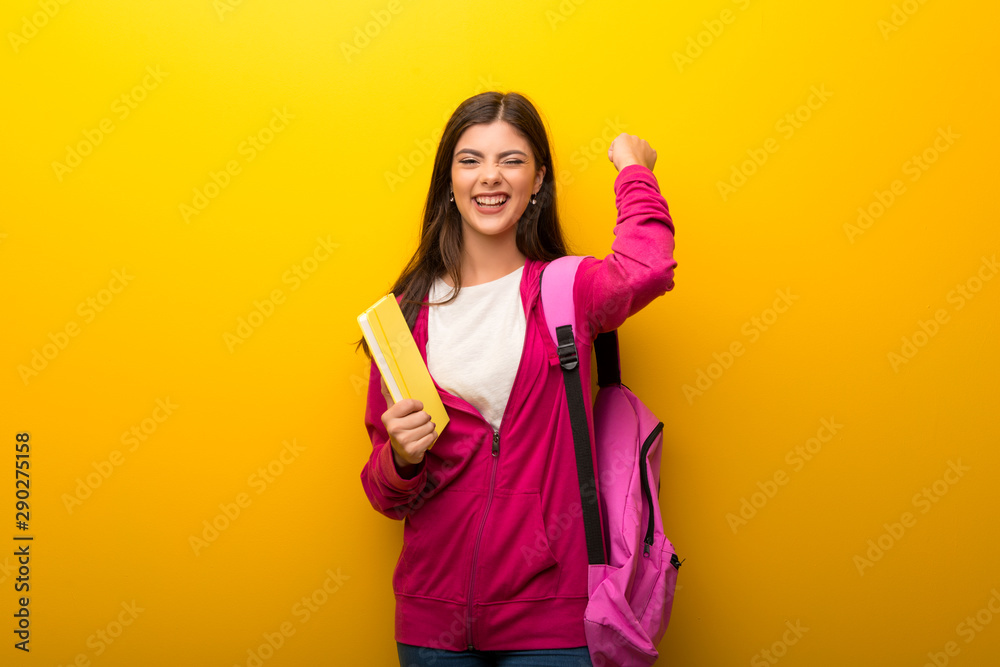 Teenager student girl on vibrant yellow background celebrating a victory Teenager student girl on vibrant yellow background celebrating a victory
