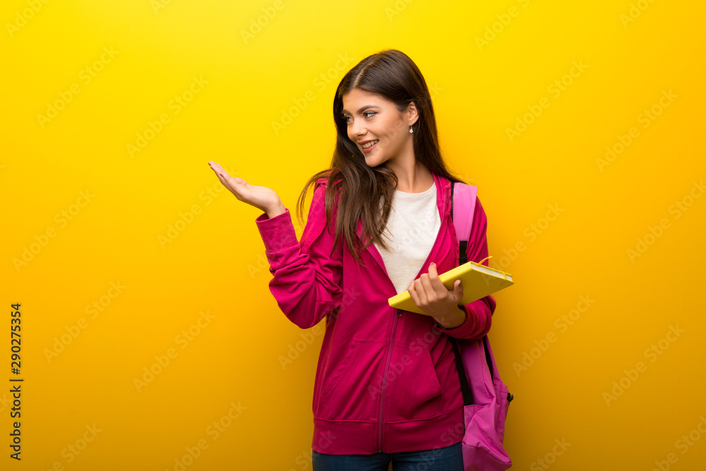 Teenager student girl on vibrant yellow background holding copyspace imaginary on the palm Teenager student girl on vibrant yellow background holding copyspace imaginary on the palm