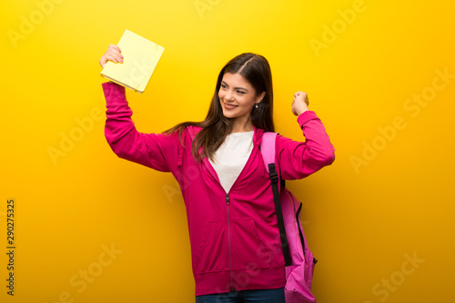 Teenager student girl on vibrant yellow background listening to the music and dancing