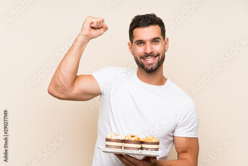 Handsome man holding muffin cake over isolated background celebrating a victory