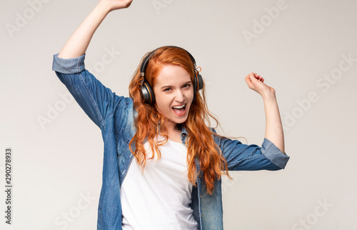 Happy ginger girl in headphones listening to music and dancing.