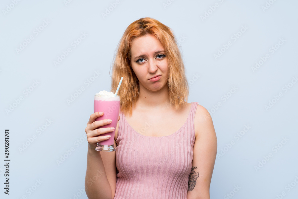 Young woman with strawberry milkshake over isolated blue background with sad expression Young woman with strawberry milkshake over isolated blue background with sad expression