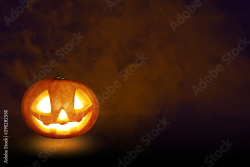 Pumpkin Jack O Lantern on a stone and under a tree with the sky is creepy background
