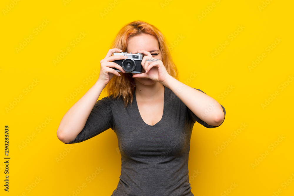 Young woman over isolated yellow background holding a camera Young woman over isolated yellow background holding a camera