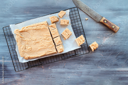 Block of delicious, homemade peanut butter fudge being cut into squares over a textured wood table background with old knife. Image shot from above.