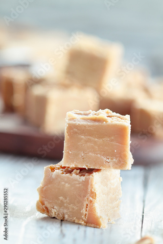Squares of delicious, homemade peanut butter fudge over a rustic wood table. Selective focus on candy in the foreground with blurred background.