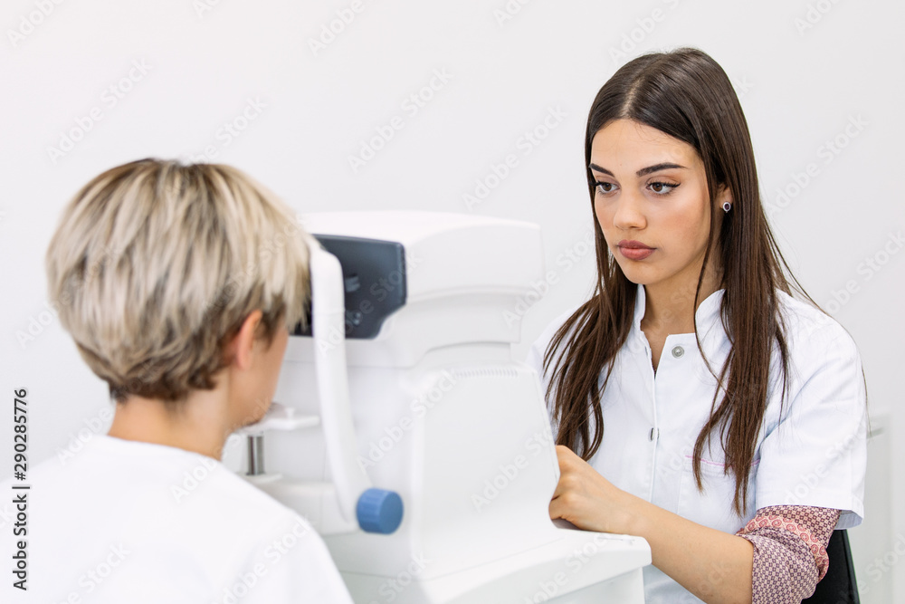 Pleasant woman with blue eyes having her eyes checked in binocular apparatus the oculist in eyes clinic doing cornea and retina exam diagnostic high technology concept eyes care Pleasant woman with blue eyes having her eyes checked in binocular apparatus the oculist in eyes clinic doing cornea and retina exam diagnostic high technology concept eyes care