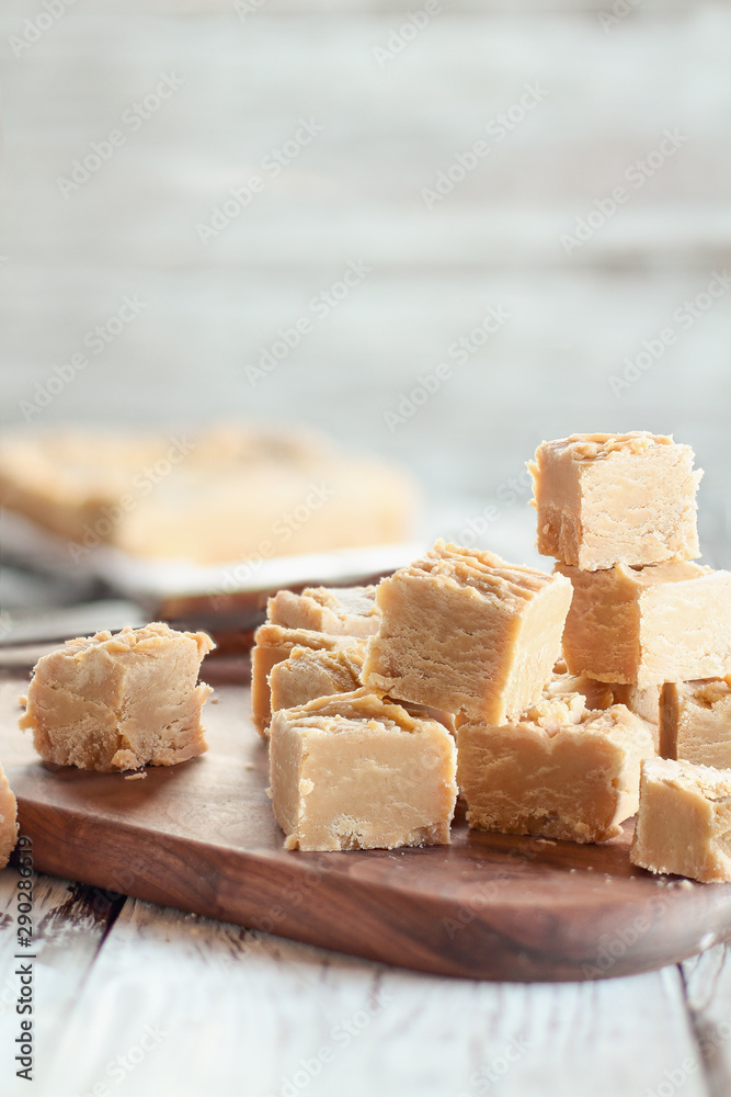 Squares of delicious, homemade peanut butter fudge over a rustic wood table. Selective focus on candy in the foreground with blurred background.