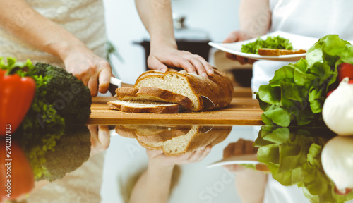 Closeup of human hands cooking in kitchen. Mother and daughter or two female friends cutting bread for dinner. Friendship, family and lifestyle concepts