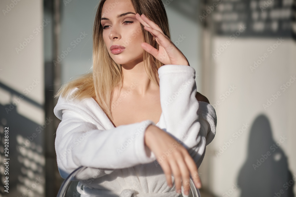 Fototapeta premium girl in a white bathrobe sits on the balcony