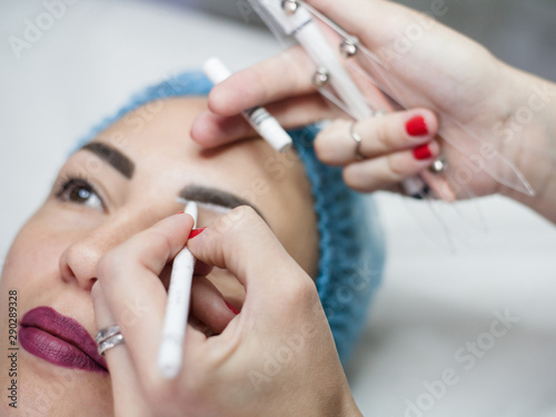 Permanent makeup. Closeup of female beautician hand sketching up symmetrical eyebrows.
