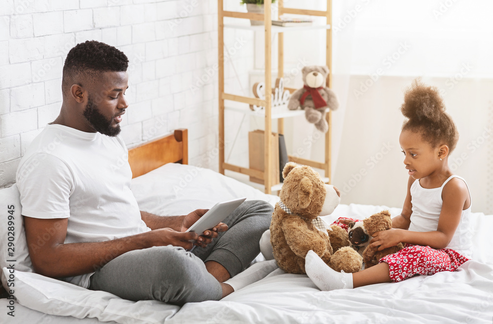 Busy african man browsing on tablet, sad little girl playing with toys alone Busy african man browsing on tablet, sad little girl playing with toys alone