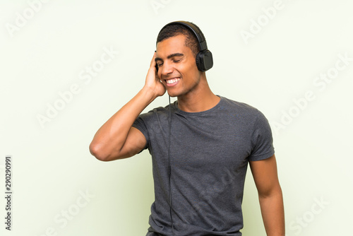 Young handsome man listening music with a mobile over isolated green wall © luismolinero