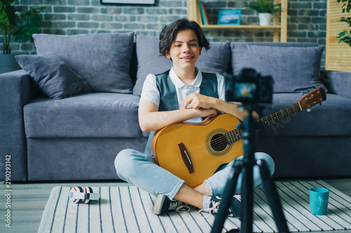 Teenage boy young vlogger is recording video for online vlog holding guitar talking smiling using modern camera. People, youth and vlogging concept. photo