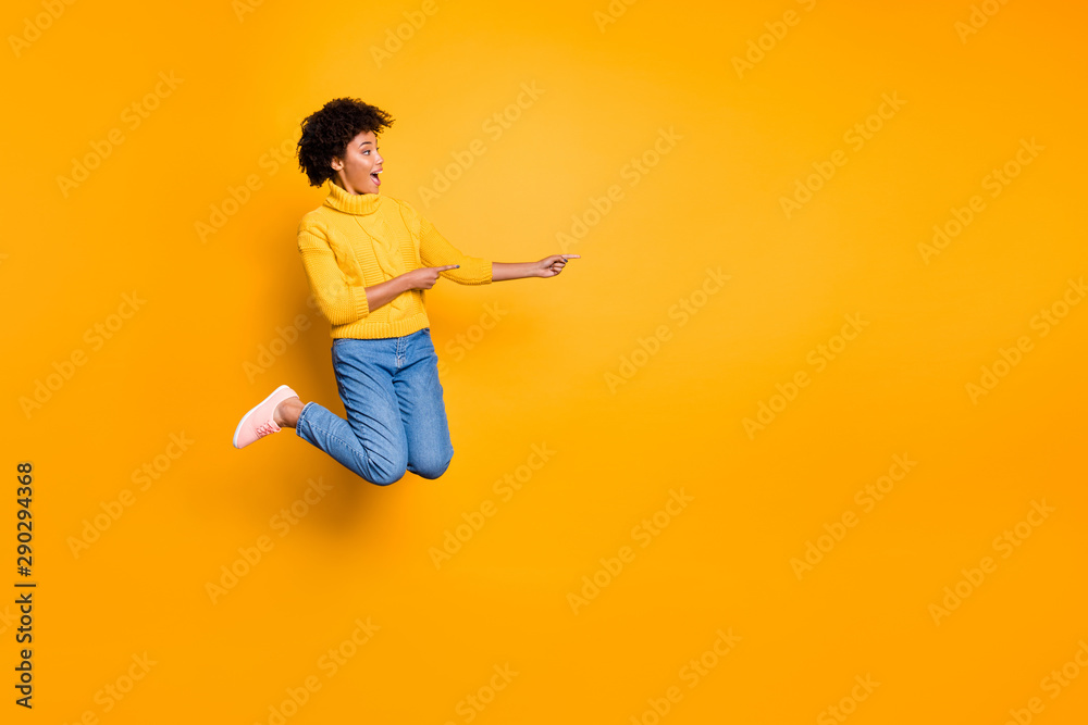 Full length body size copyspace photo of stylish trendy model pretty sweet charming girlfriend pointing at emptiness jumping up adverting wearing jeans denim pullover isolated vibrant color background