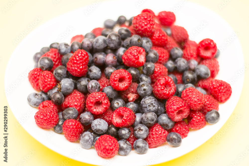 Forest berries, raspberries, blueberries in a bowl on a yellow background from above Forest berries, raspberries, blueberries in a bowl on a yellow background from above