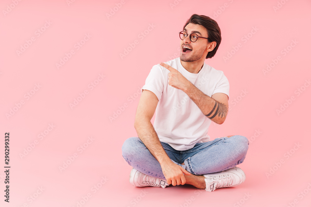 Image of young man pointing finger at copyspace while sitting on floor Image of young man pointing finger at copyspace while sitting on floor
