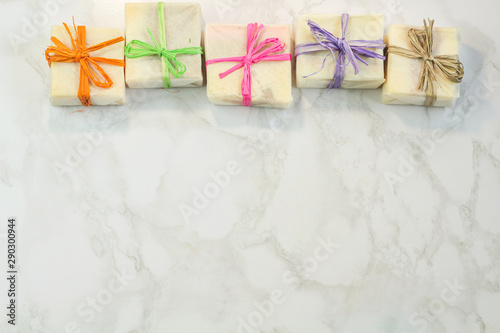 handmade organic soap in gift wax wrapping  paper with multi colored eco raffia ribbons on marble surface with space for text. Instagram style soap flat lay frame