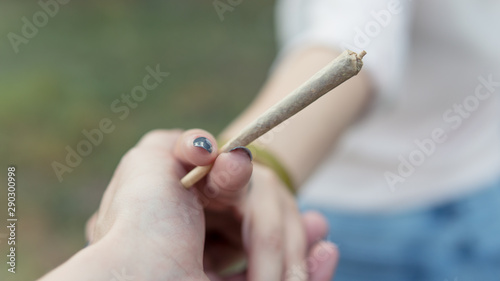 Close-up of females hands holding marijuana joint, smoking cannabis blunt outdoors.